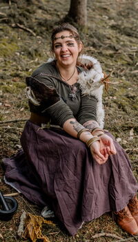 Eine lächelnde Frau in historischer Kleidung sitzt im Wald und verkörpert die Gemeinschaft der Turngemeinde Landshut.