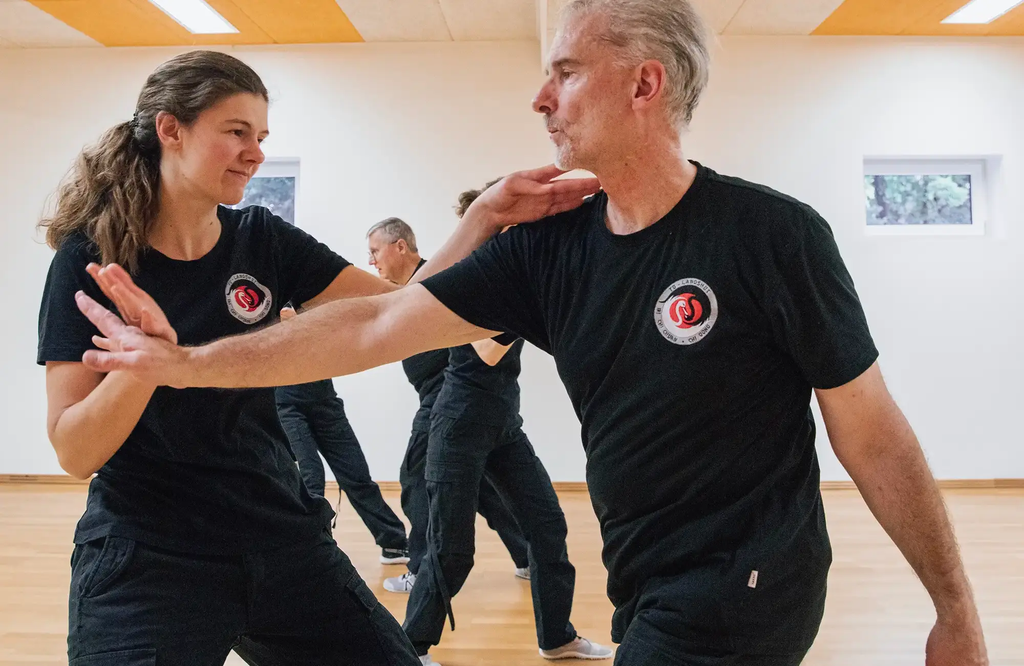 Zwei Personen üben Kampfkunsttechniken in einem Raum der Turngemeinde Landshut, mit Fokus auf präzise Bewegungen.