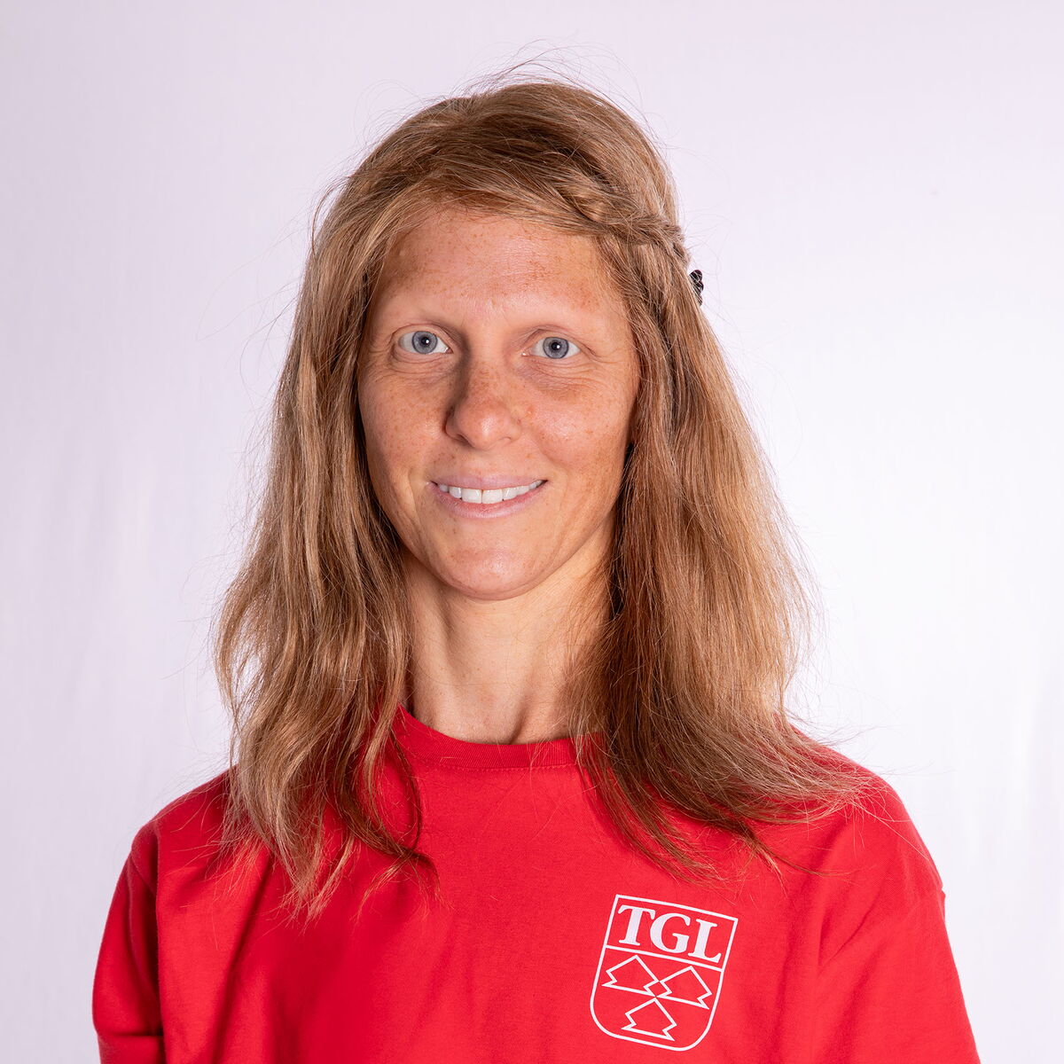 Eine Frau in einem roten TGL-T-Shirt lächelt freundlich in die Kamera, stolz Teil des Sportvereins zu sein.
