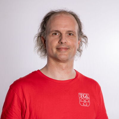 Ein Mann in einem roten TGL-Shirt der Turngemeinde Landshut lächelt vor einem neutralen Hintergrund.