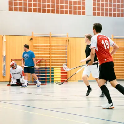In einer Sporthalle spielt eine Gruppe von Männern Floorball, darunter ein Spieler mit einem Trikot der Turngemeinde Landshut.