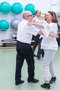 Ein älteres Paar tanzt lachend in einem Sportraum des Turnvereins Landshut vor bunten Gymnastikbällen.
