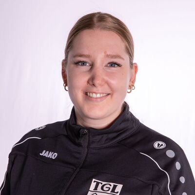 Eine lächelnde Person trägt eine schwarze Jacke mit TGL-Logo, die den Turnverein Landshut repräsentiert.