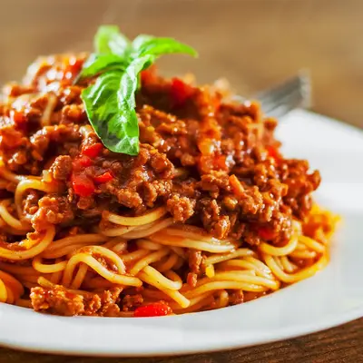 Ein leckeres Spaghetti-Bolognese-Gericht wird auf einem weißen Teller serviert, perfekt für das nächste TGL-Vereinstreffen.