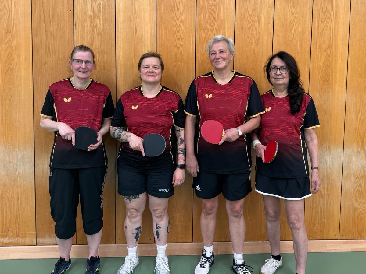 Fünf Frauen in Turngemeinde-Trikots posieren mit Tischtennisschlägern vor einer Holzvertäfelung.