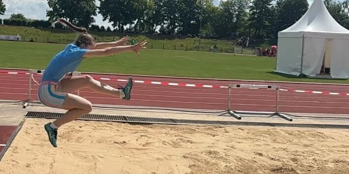 Eine Sportlerin von der Turngemeinde springt beim Weitsprung kraftvoll in die Sandgrube auf einem sonnigen Sportplatz.