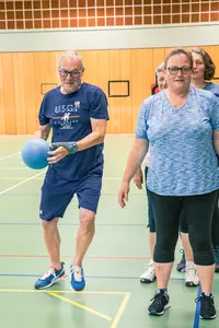 Ein Mann spielt in einer Sporthalle der Turngemeinde Landshut mit einem blauen Ball, während andere zuschauen.