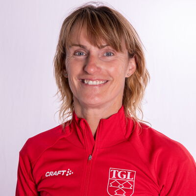 Eine lächelnde Frau trägt eine rote TGL-Jacke, symbolisierend den Sportgeist des Vereins Turngemeinde Landshut.