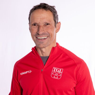 Eine lächelnder Mann trägt eine rote TGL-Jacke, symbolisierend den Sportgeist des Vereins Turngemeinde Landshut.
