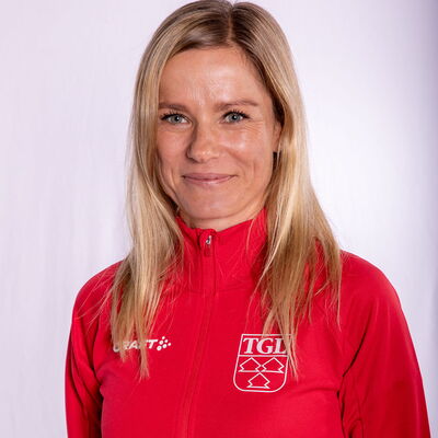 Eine lächelnde Frau trägt eine rote TGL-Jacke, symbolisierend den Sportgeist des Vereins Turngemeinde Landshut.