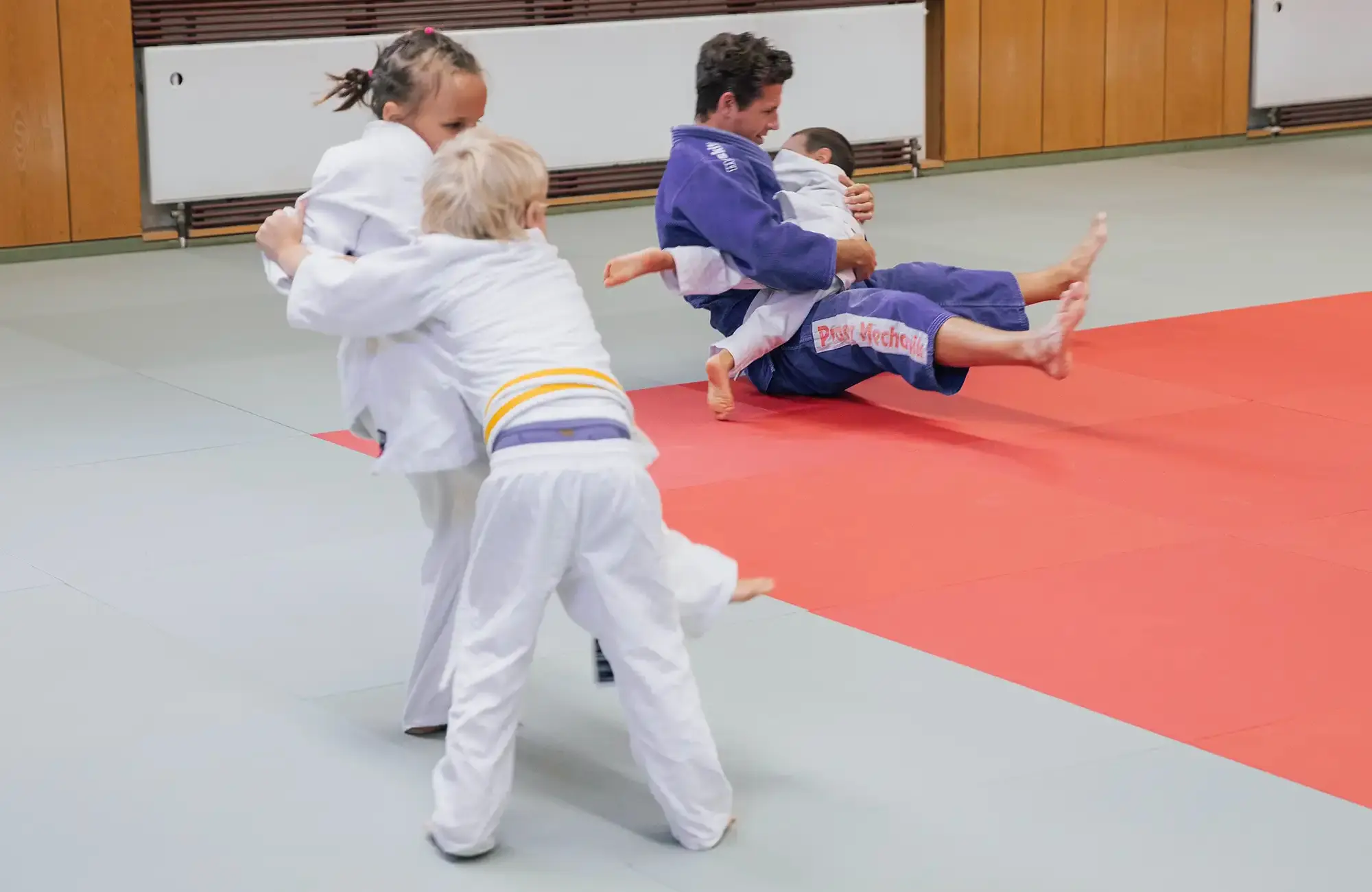 Kinder trainieren Judo auf einer Matte im Sportverein Turngemeinde Landshut unter Anleitung eines Trainers.