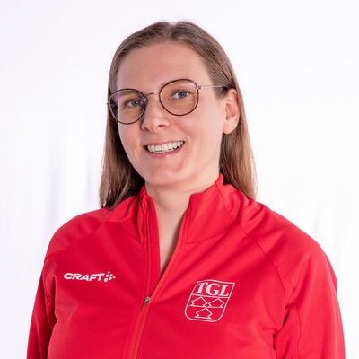 Eine lächelnde Frau trägt eine rote TGL-Jacke, symbolisierend den Sportgeist des Vereins Turngemeinde Landshut.