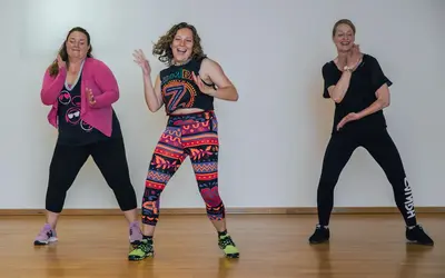 Drei Frauen tanzen fröhlich in einem Sportkurs der Turngemeinde Landshut und genießen die gemeinsame Bewegung.