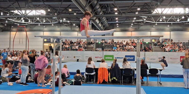 Ein Turner der Turngemeinde Landshut zeigt eine beeindruckende Barrenübung vor einem gespannten Publikum.