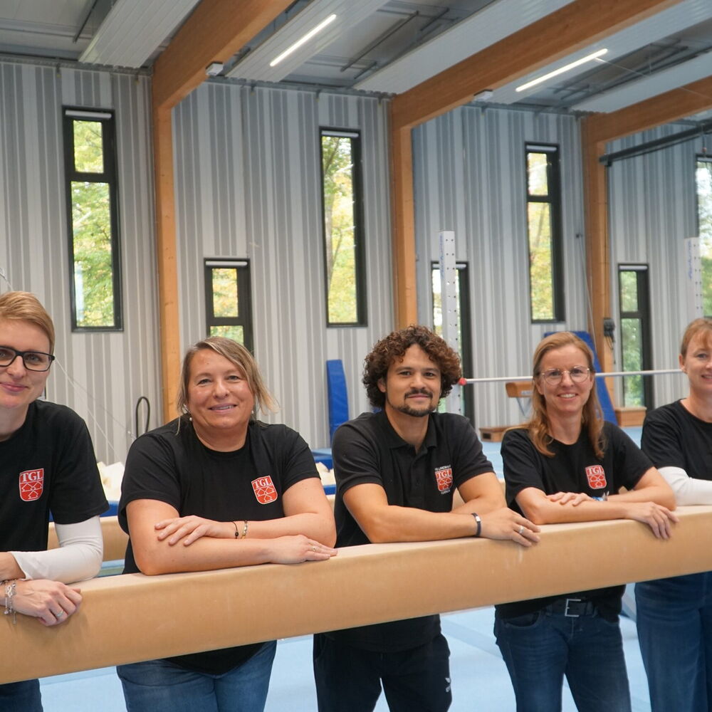 Fünf Übungsleiter in TGL-Shirts in der Turnhalle der TGL.