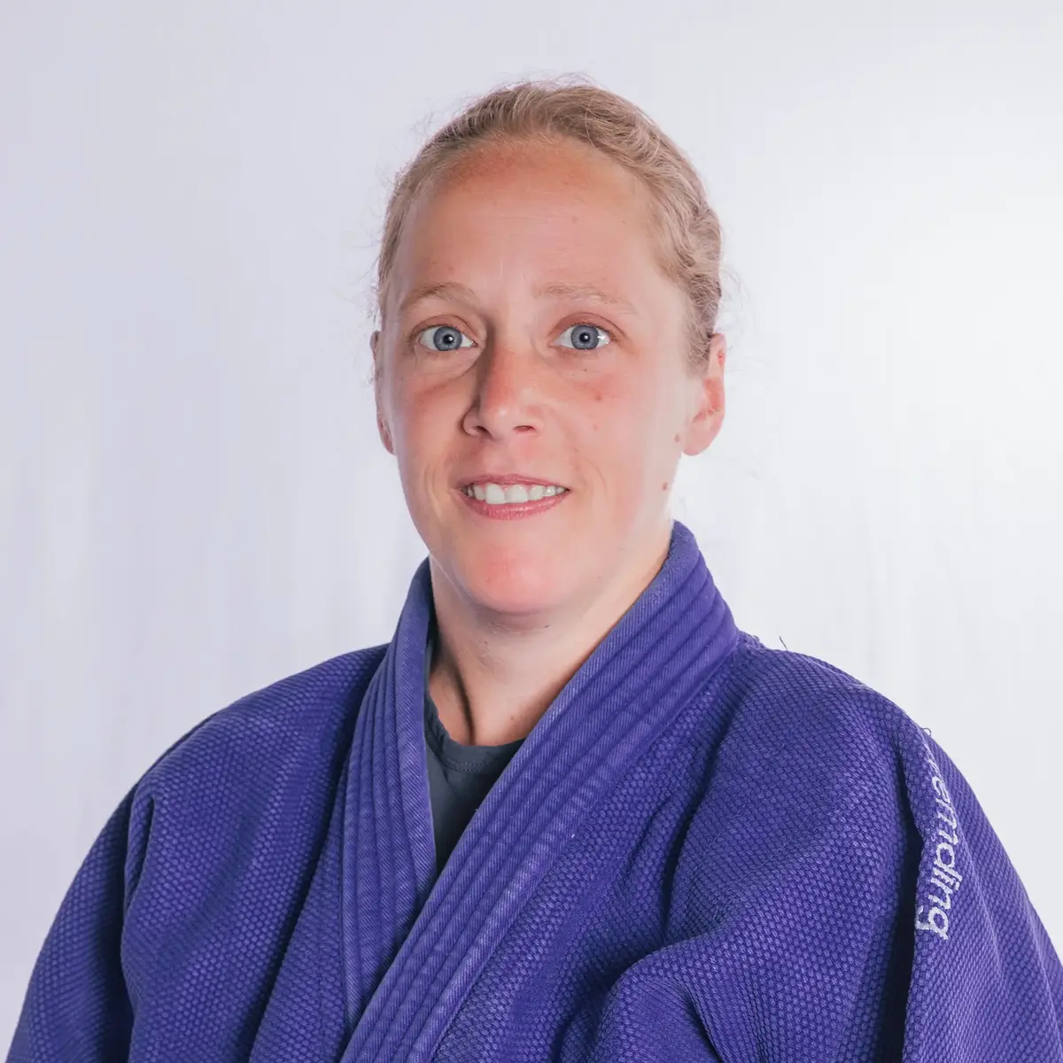 Eine Frau in einem blauen Judoanzug lächelt in die Kamera, repräsentiert den Sportverein Turngemeinde Landshut.