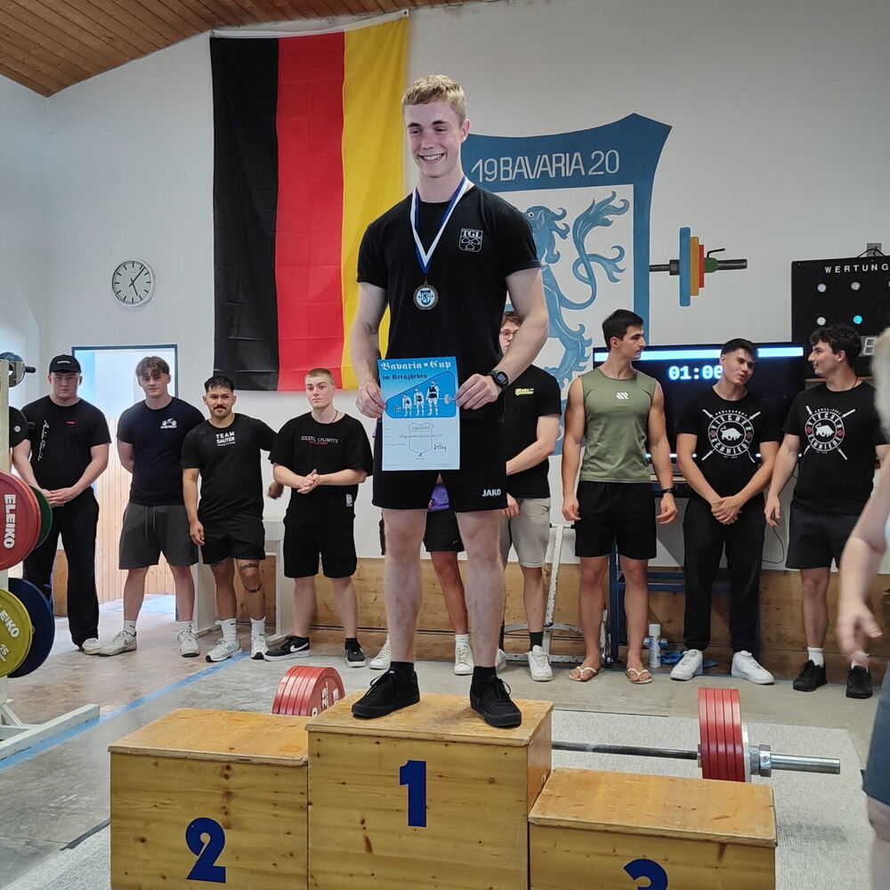Ein Sportler der Turngemeinde Landshut steht auf dem Siegertreppchen mit einer Medaille und einer Urkunde in der Hand.