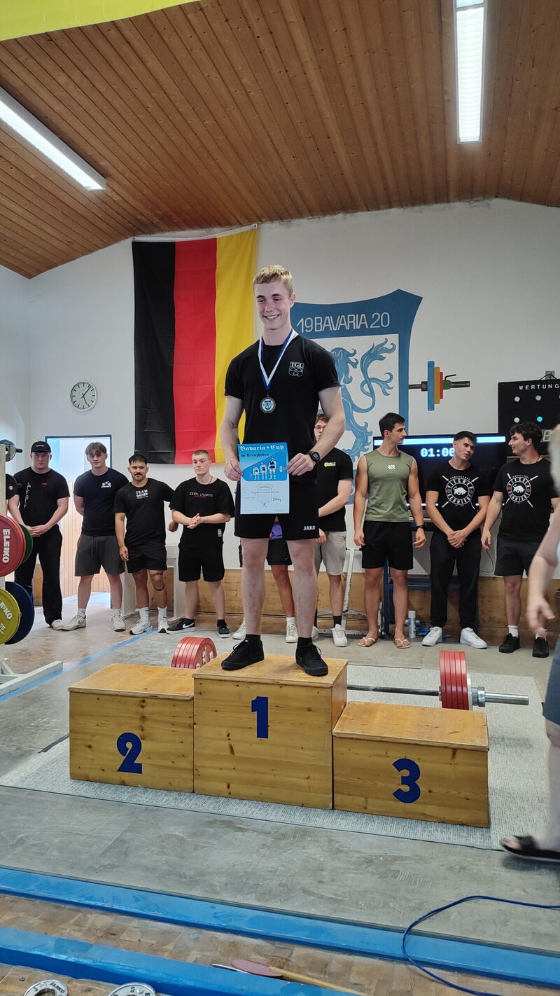 Ein Sportler der Turngemeinde Landshut steht auf dem Siegertreppchen mit einer Medaille und einer Urkunde in der Hand.
