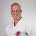 Ein Mann in Karateanzug mit dem Logo der TG Landshut steht vor neutralem Hintergrund.