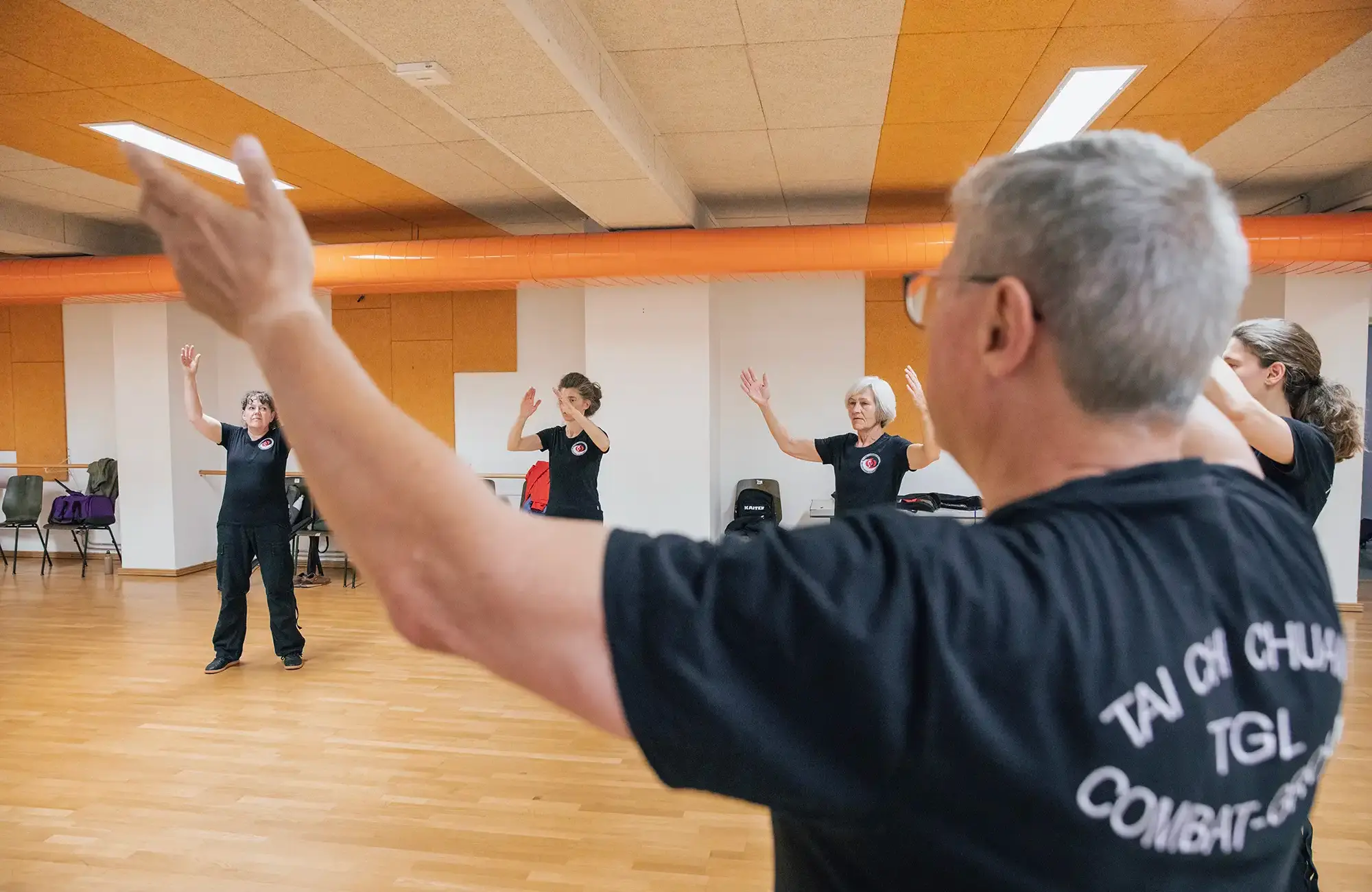 Teilnehmer üben Tai Chi in einem Raum der Turngemeinde Landshut, während ein Trainer die Bewegungen anleitet.