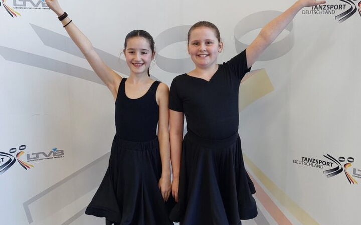 Zwei junge Tänzerinnen in schwarzen Kleidern posieren stolz beim Tanzsportwettbewerb für den Verein Turngemeinde Landshut.