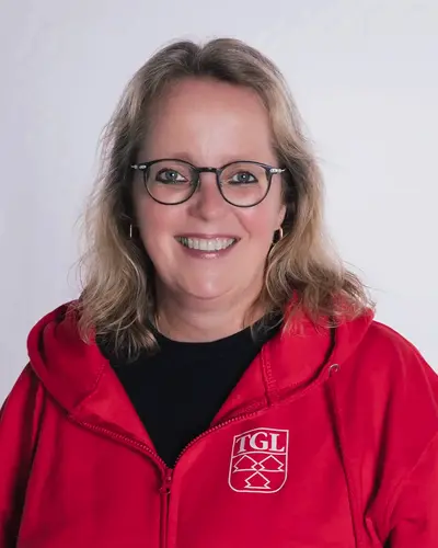 Ulrike Aigner lächelt in die Kamera, während sie eine rote Jacke mit dem Logo des Turngemeinde Landshut Vereins trägt.