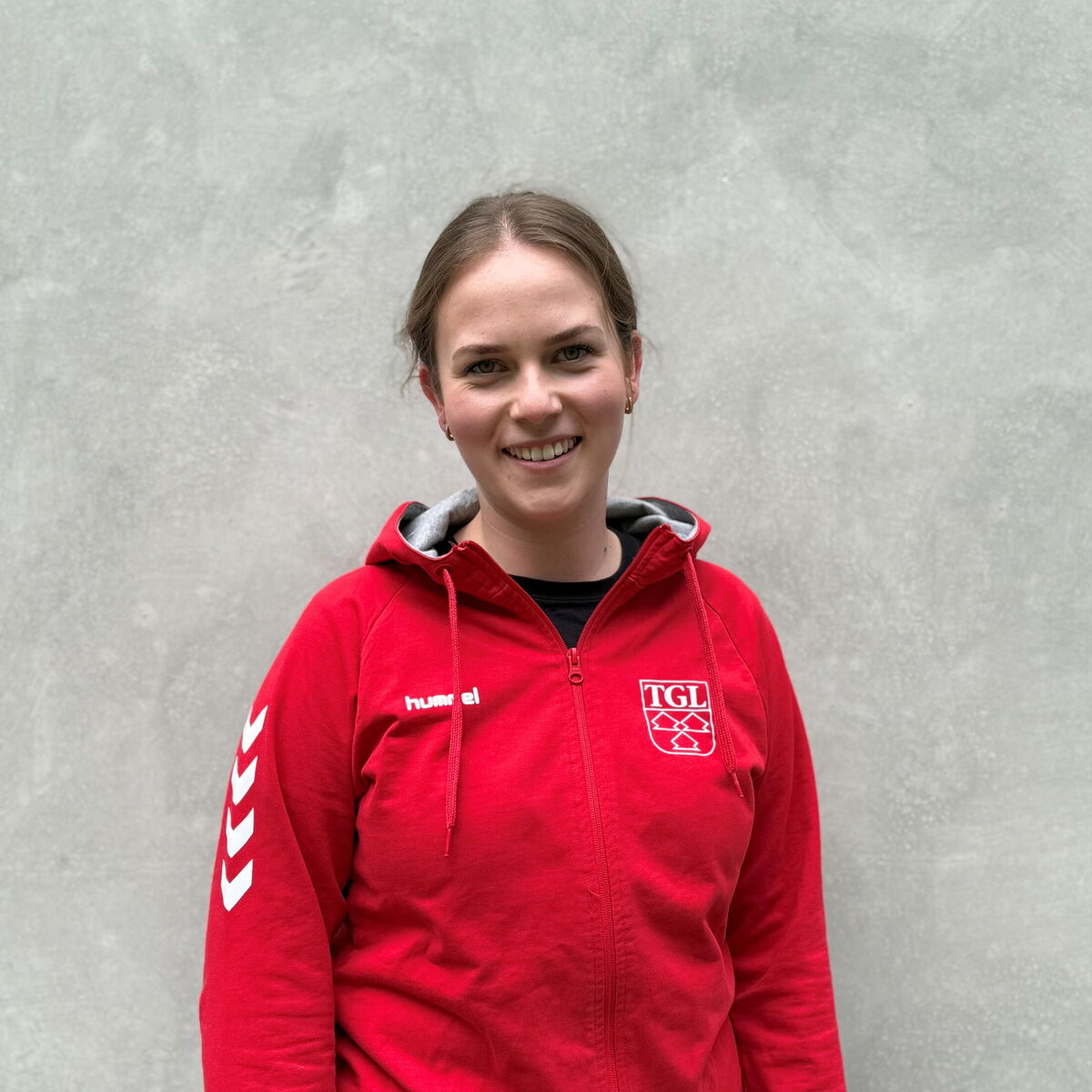 Eine junge Frau im roten TGL-Shirt lächelt freundlich in die Kamera, repräsentativ für den Verein in Landshut.