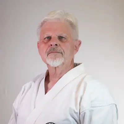 Ein älterer Mann in einem Karateanzug mit dem Logo der Turngemeinde Landshut steht vor einem neutralen Hintergrund.