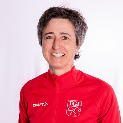 Eine lächelnde Frau trägt eine rote TGL-Jacke, symbolisierend den Sportgeist des Vereins Turngemeinde Landshut.