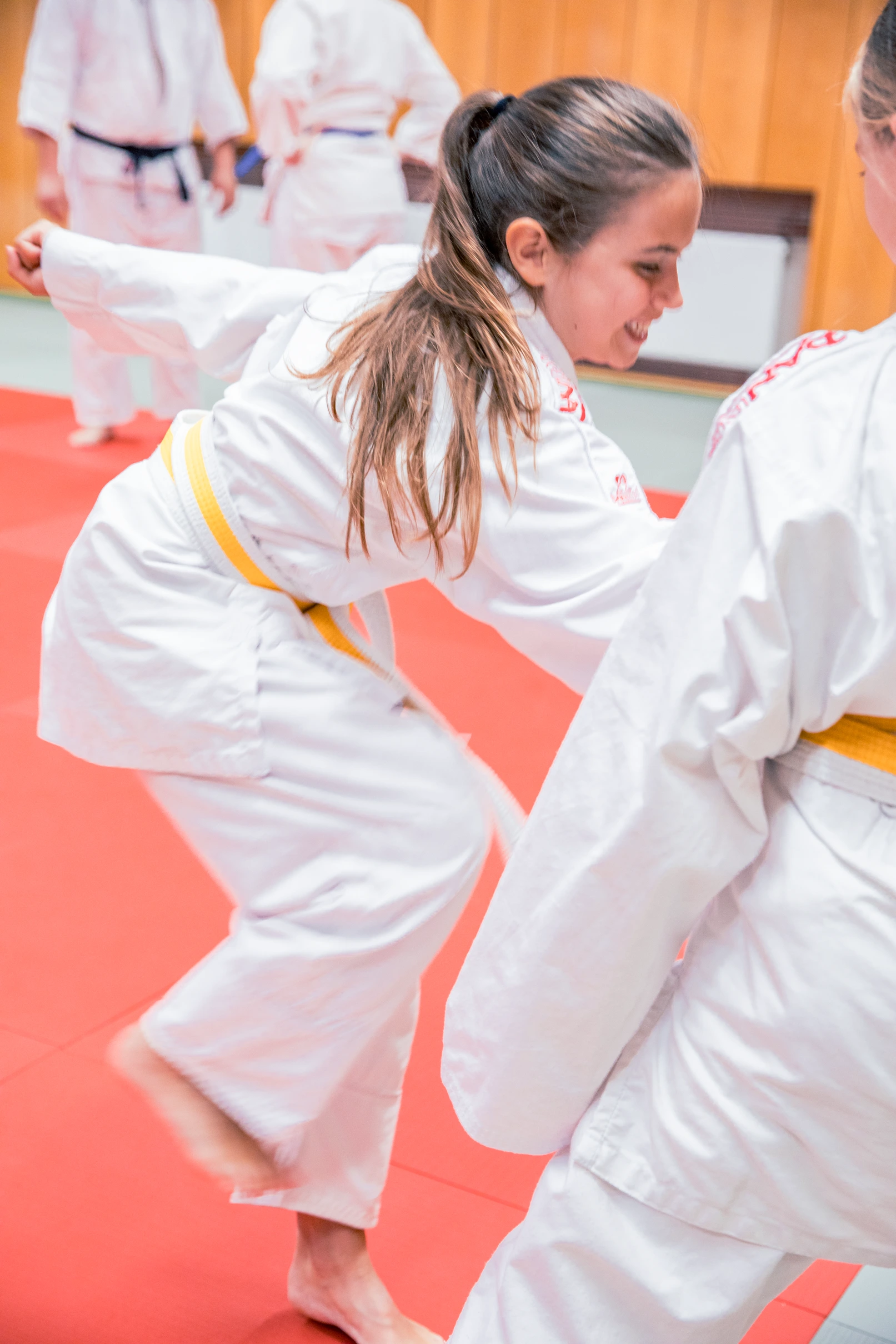 Zwei junge Judoka trainieren auf einer roten Matte im Sportverein, während sie konzentriert Techniken üben.