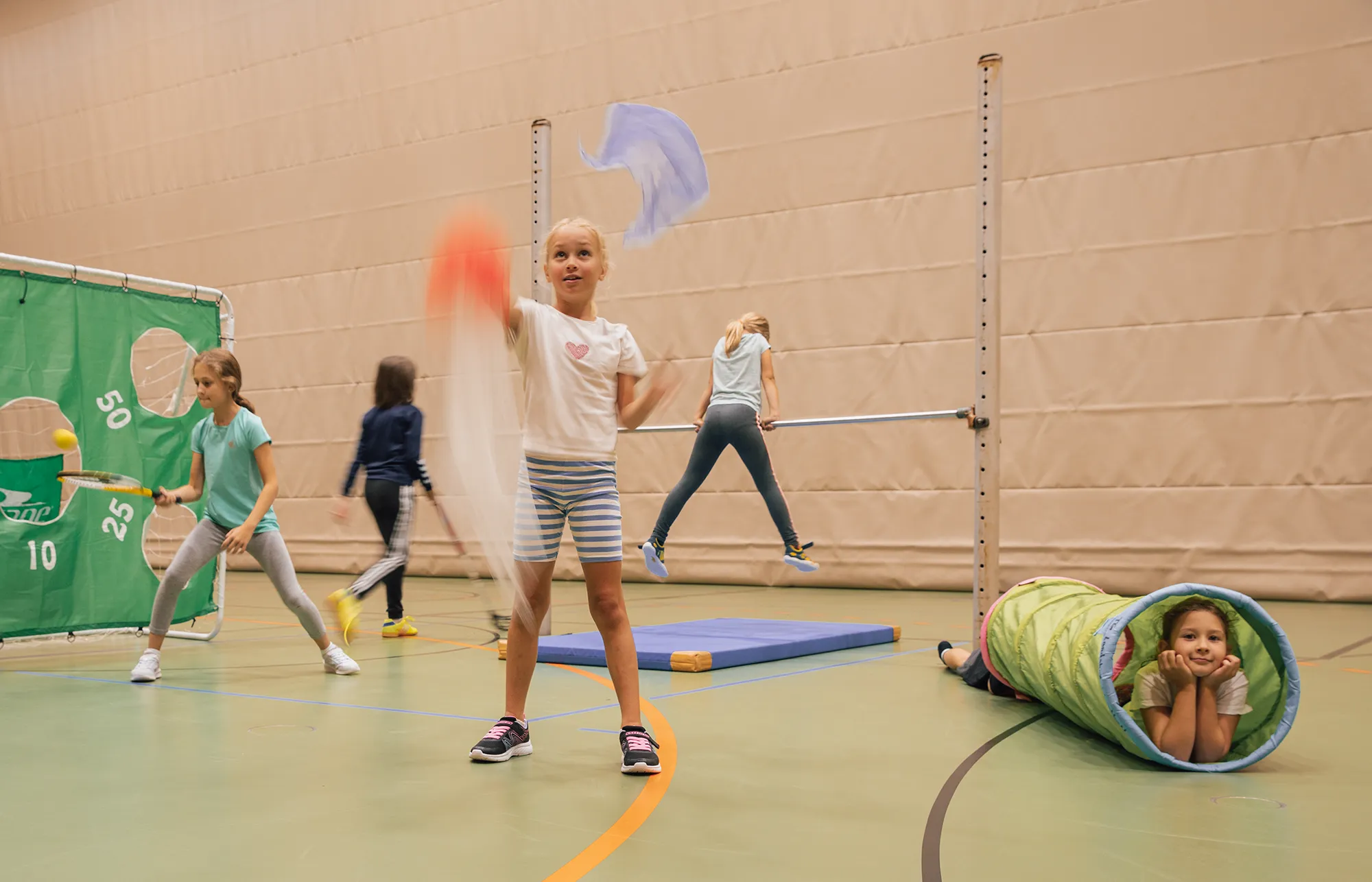 Kinder der Turngemeinde Landshut spielen fröhlich in einer Sporthalle mit bunten Tüchern und Geräten.