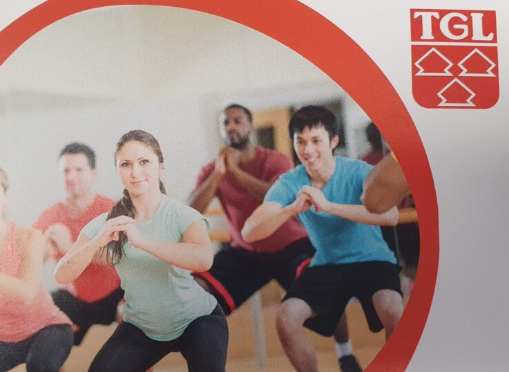 Eine Gruppe von Menschen macht Fitnessübungen im Vereinszentrum der Turngemeinde Landshut, erkennbar am TGL-Logo.