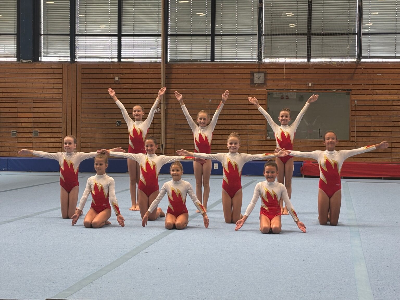 Eine Gruppe junger Turnerinnen der TG Landshut posiert stolz in einer Sporthalle nach ihrer beeindruckenden Leistung.