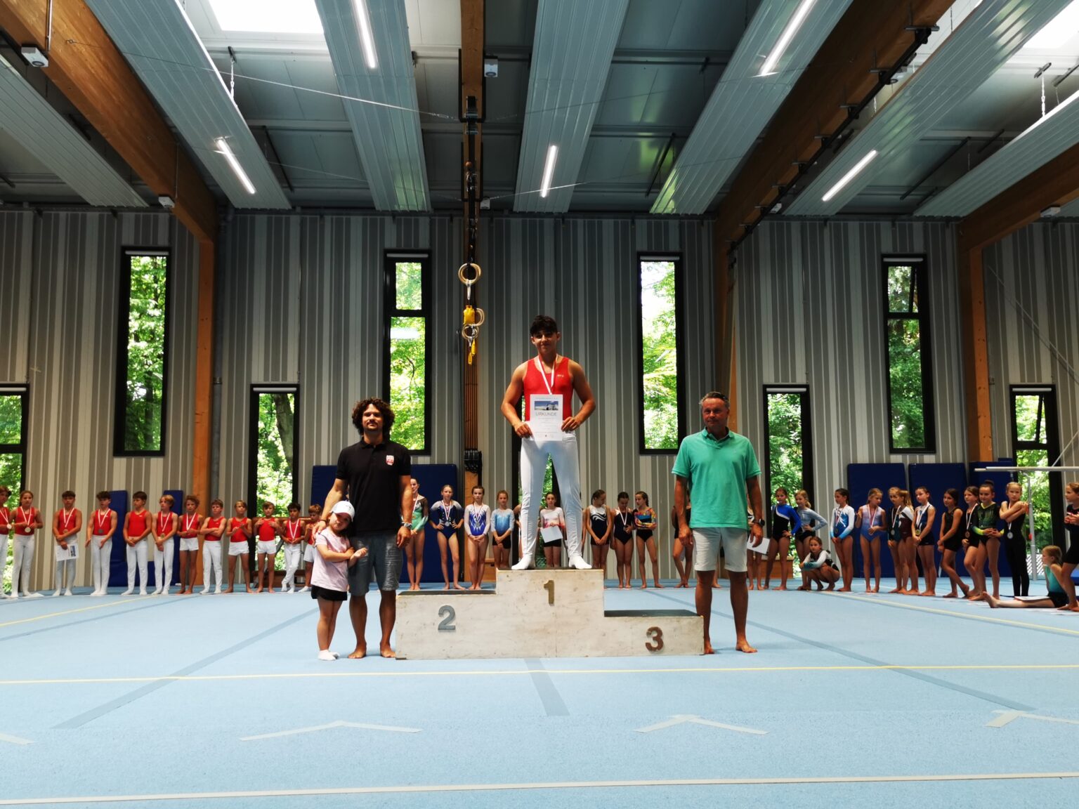 Ein Junge steht stolz auf dem Siegertreppchen bei einem Turnwettbewerb der Turngemeinde Landshut.