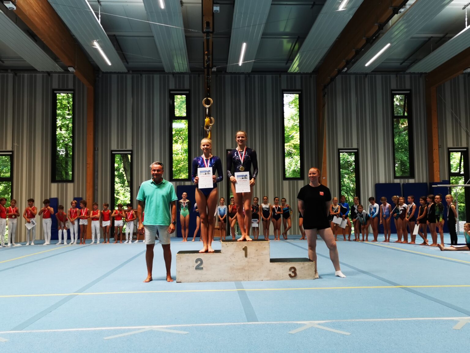 Ein Mädchen steht auf dem Siegerpodest bei einem Turnwettbewerb der Turngemeinde Landshut, umgeben von anderen Teilnehmern.